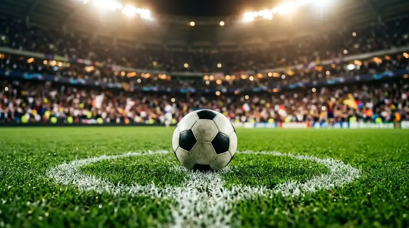 A close-up of a football on the penalty spot under stadium floodlights, the arena softly blurred behind