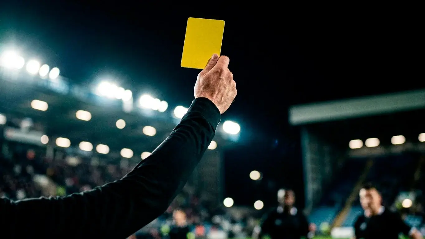 A football referee holding up a yellow card under floodlights